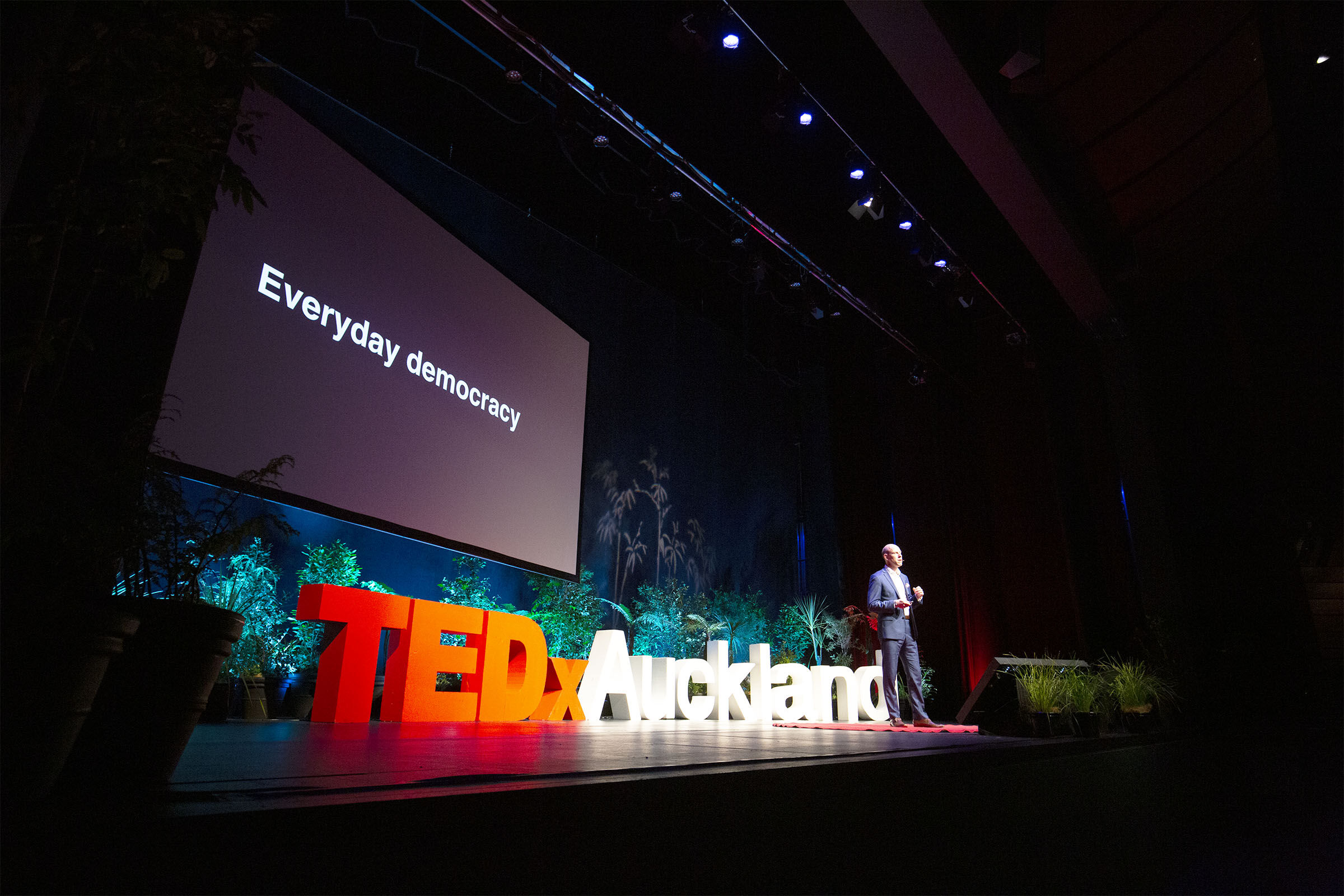 Max on stage at TEDx with 'Everyday Democracy' slide on screen behind